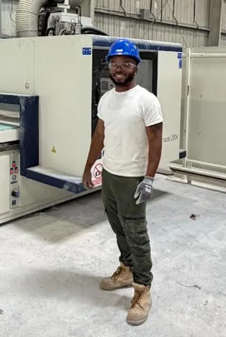 A FullStack Modular team member in a hard hat and safety glasses standing beside machinery on the factory floor